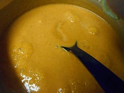 Overhead View of Boiling Soup in a Pan and a Black Ladel on the Right Inserted For Stirring