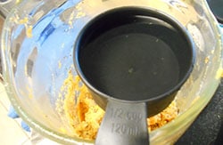 Overhead View of 1/2 Cup Measuring Cup Filled with Water Hovering over Blended Sweet Potato in a Blender