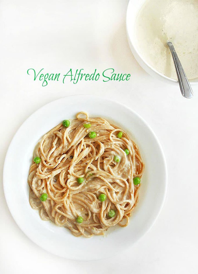 Overhead View of A Bowl of Spaghetti with Vegan Alfredo Sauce. In the Background, There is a White Bowl Filled with th Alfredo Sauce and a Stainless Spoon In it