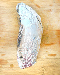 A Sweet Potato Wrapped in Aluminium Foil placed on top of a chopping block - 5 Tips on Baking The Perfect Sweet Potato