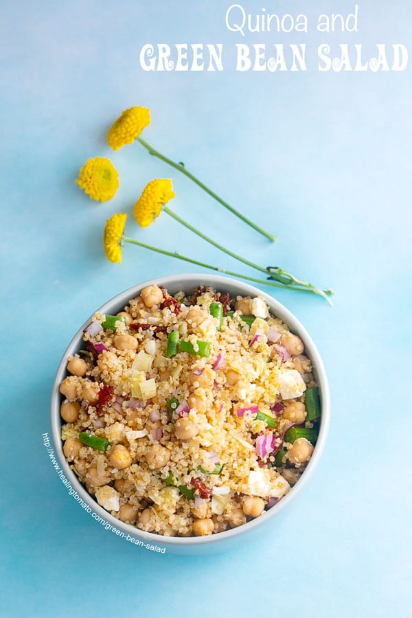 Overhead view of a bowl on a blue background. Bowl is filled with quinoa, green beans and chick peas. No Garnish. Small yellow carnations on the side - Green Bean Salad