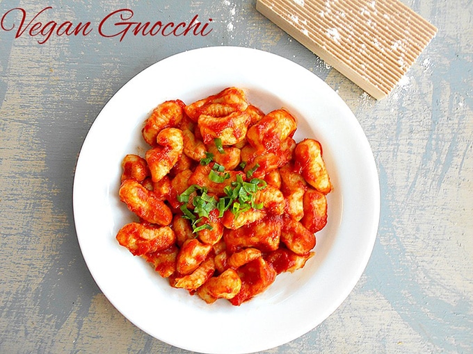 Overhead View of a White Plate Filled With Gnocchi in a Red Pasta Sauce. There is a Lightly Floured Gnocchi Board Next to the Plate