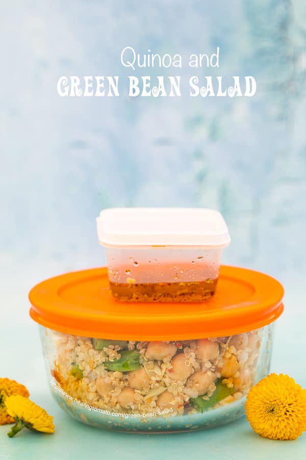 Front view of a round glass meal prep bowl with orange lid filled with the green bean salad. On top of the bowl is a small plastic container filled with the orange dressing 