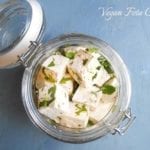 overhead photo of feta cheese in a glass jar on a blue surface