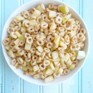 Overhead view of a bowl of cheerios and apples on a blue background