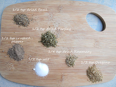 Spices used in this recipe are arranged in tiny mounds over a brown chopping board and each mound is labeled with the spice name