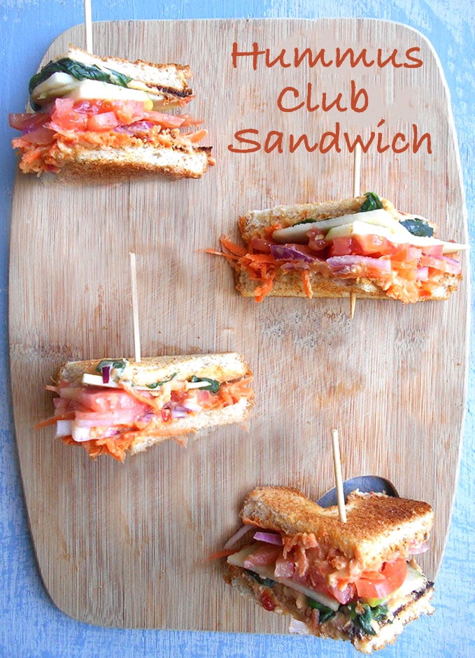 Overhead View of 4 Club Sandwiches Cut into Triangle Shapes Sitting on a Brown Cutting Board.