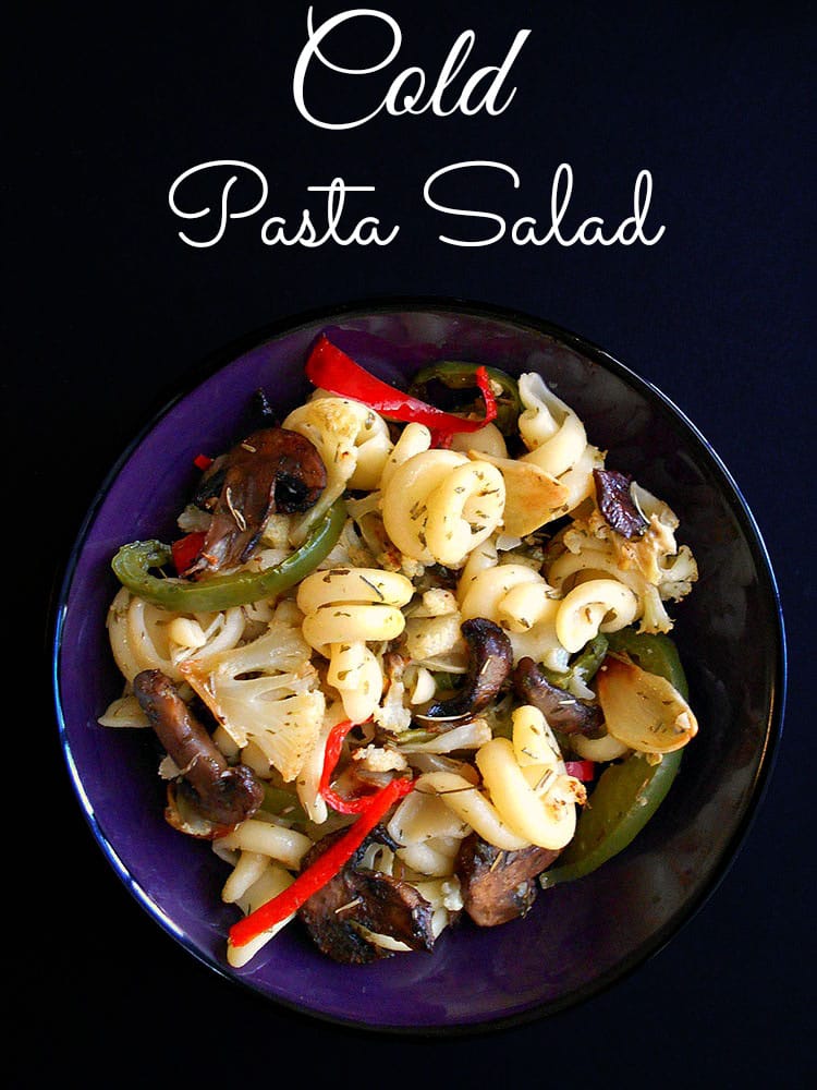 Overhead view of a dark blue bowl filled with cold pasta salad on a black background