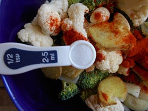 Overhead view of a ½ tsp measuring spoon filled with salt hovering over a bowl of veggies - Broccoli Soup