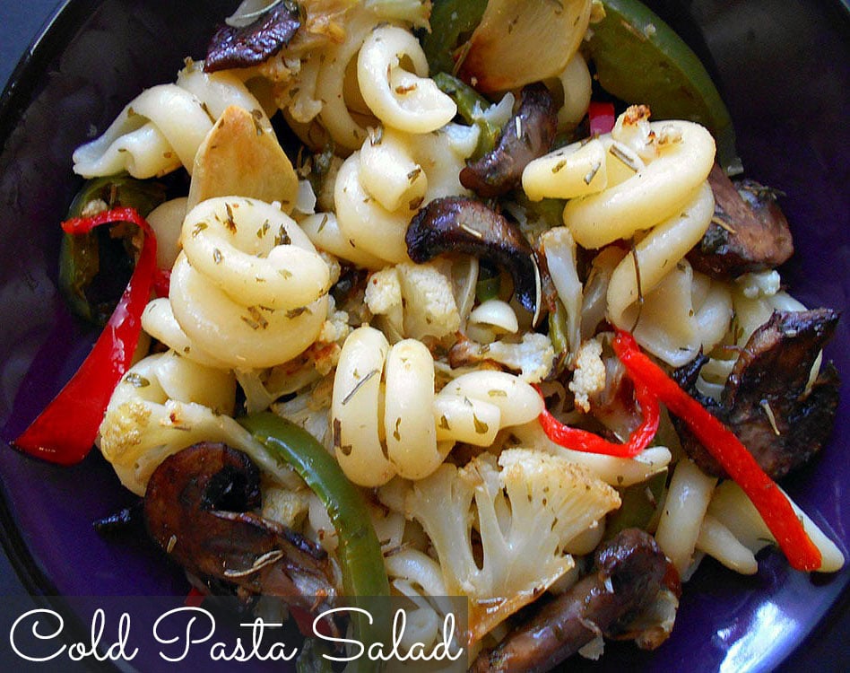 Closeup view of a dark blue bowl filled with cold pasta salad on a black background