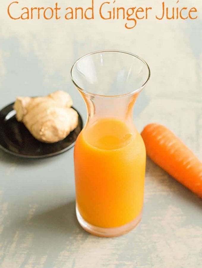 75 degree view of a small glass vase filled three quarters of the way with carrot juice. To the right of the vase in the back is a carrot and to the left is a ginger root