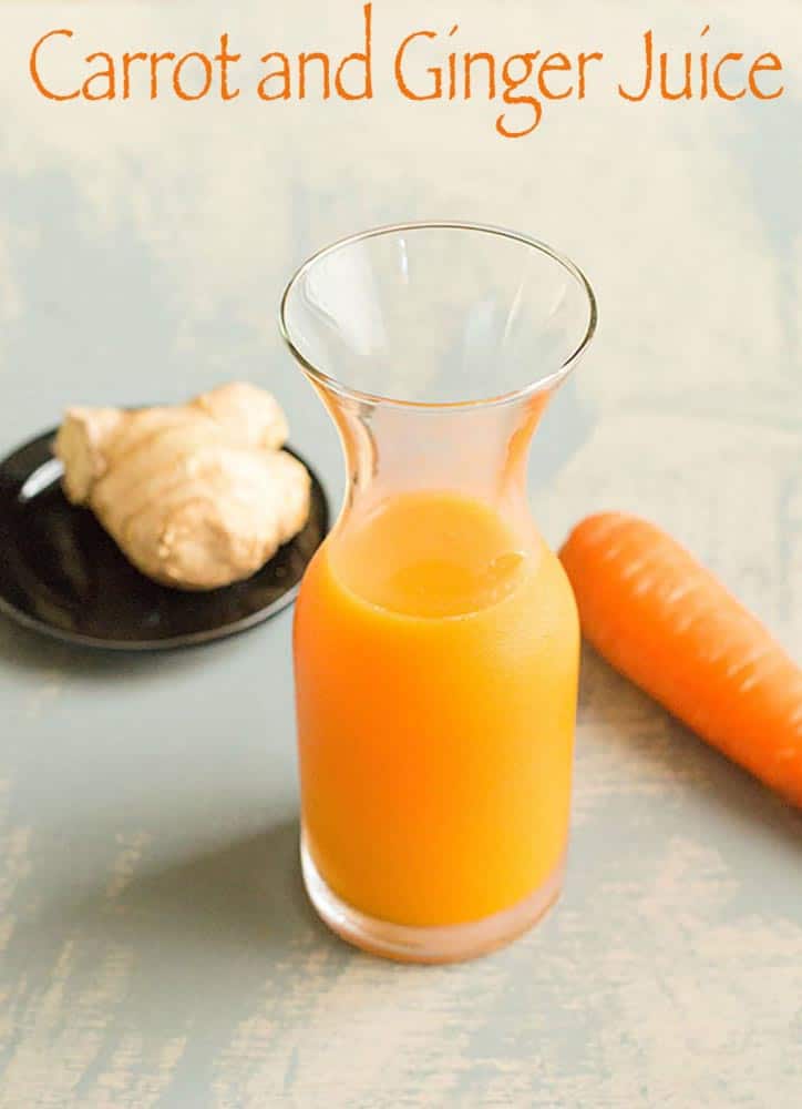 75 degree view of a small glass vase filled three quarters of the way with carrot juice. To the right of the vase in the back is a carrot and to the left is a ginger root