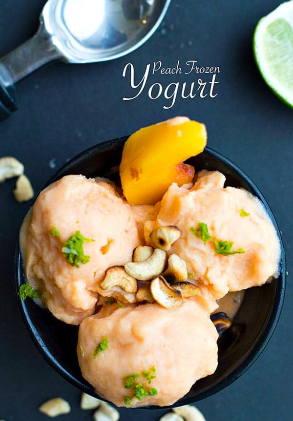 Overhead view of a bowl filled with 3 scoops of vegan peach frozen yogurt. Garnished with lime zest and roasted cashews