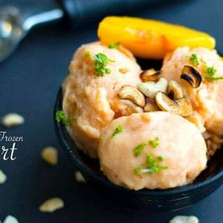 Front view of a bowl filled with 3 scoops of vegan peach frozen yogurt. Garnished with lime zest and roasted cashews