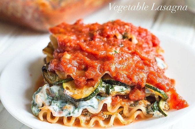 Front view of a section of vegetarian lasagna with veggies and other ingredients visible. A bottle of Bertolli pasta is blurred in the background