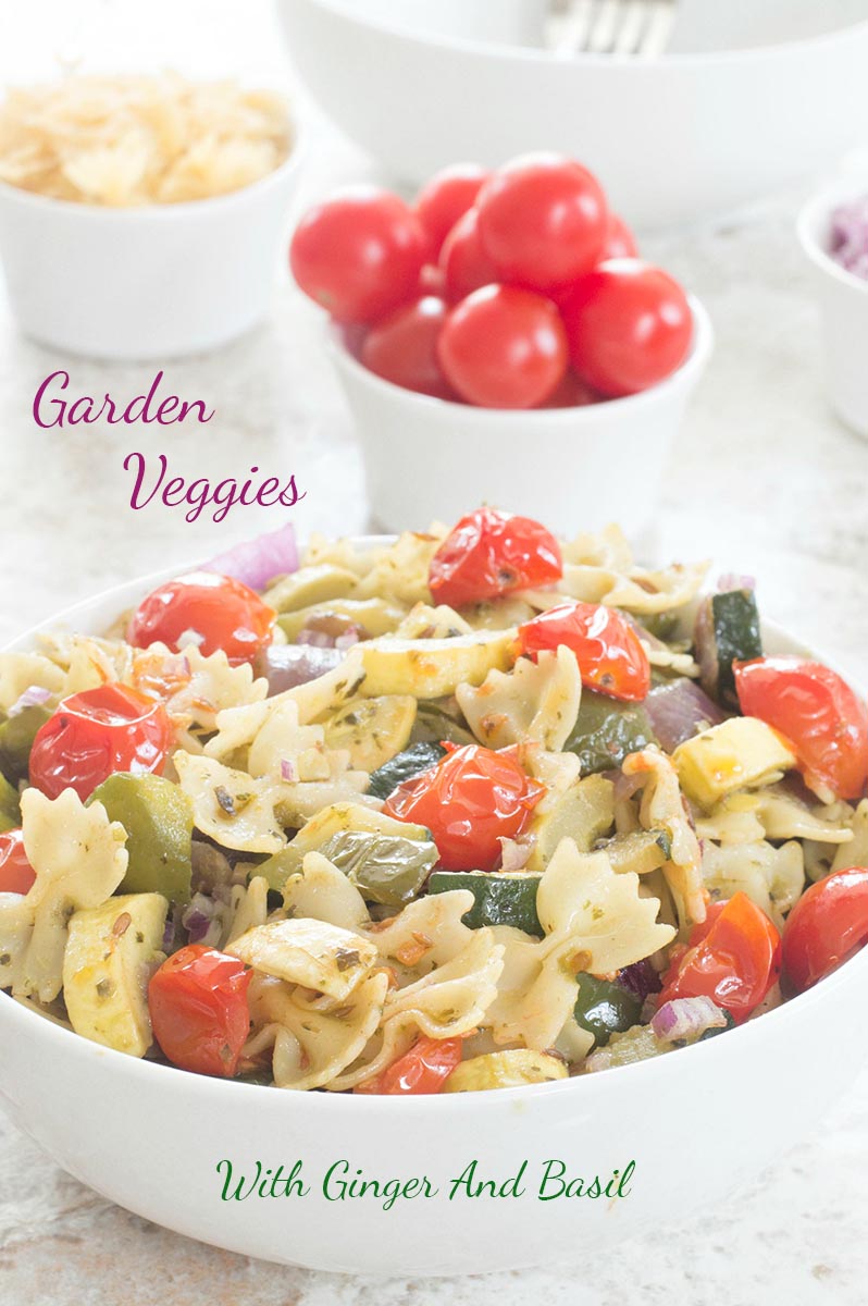 Front view of Farfalle pasta in a white bowl filled with roasted veggies. Tomatoes, pasta and onions in ramekins seen in the background