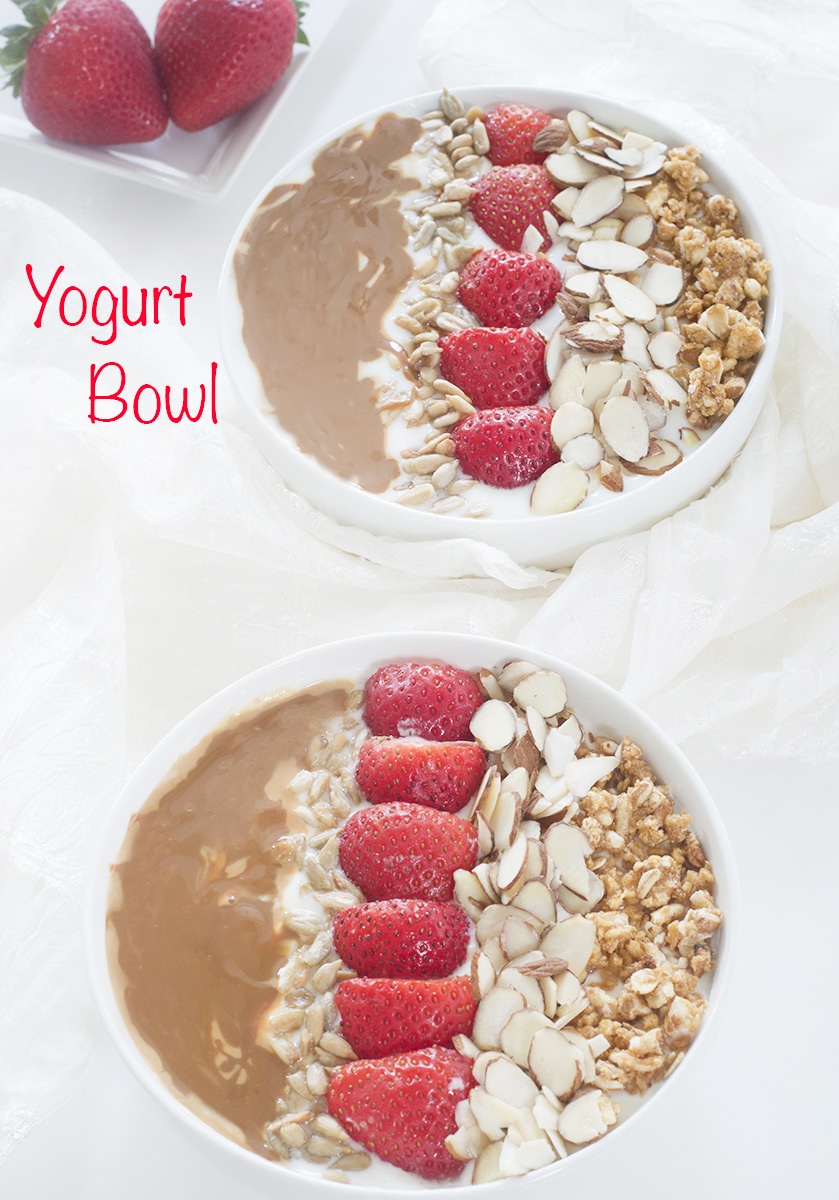 Overhead view of 2 white bowls filled with yogurt, strawberry, almonds, granola and dulce de leche - Greek Yogurt Bowl