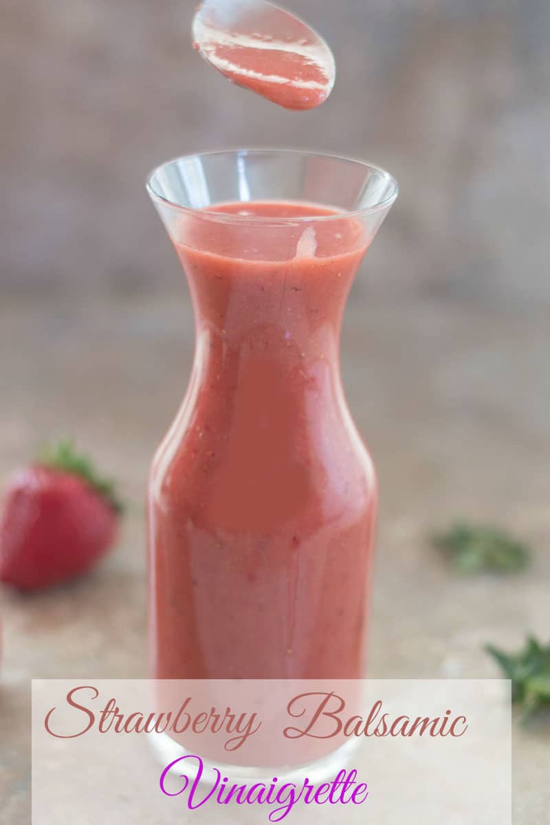 A Filled Spoon over Strawberry Balsamic Vinaigrette in a glass jar with strawberries in the background