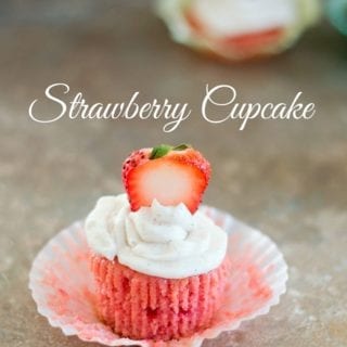 Front View of a Strawberry Cupcake With Frosting and a Sliced Strawberry. In the Background, there is One More Cupcakes