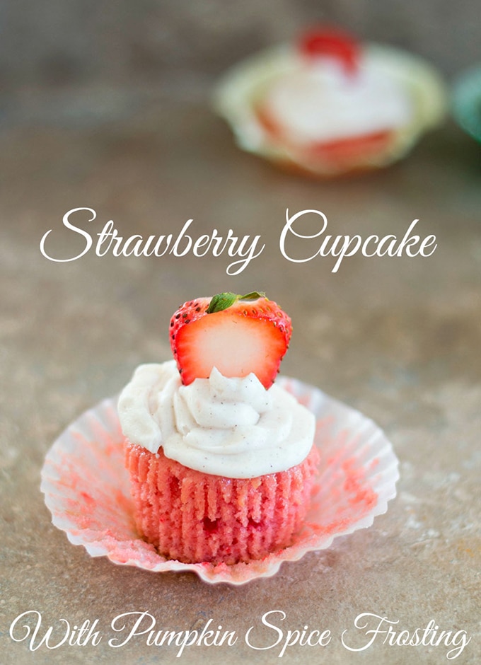 Front View of a Strawberry Cupcake With Frosting and a Sliced Strawberry. In the Background, there is One More Cupcakes