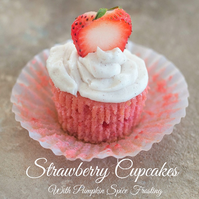 Front View of a Strawberry Cupcake With Frosting and a Sliced Strawberry. The Liner has been Peeled Away to Reveal the Cupcake