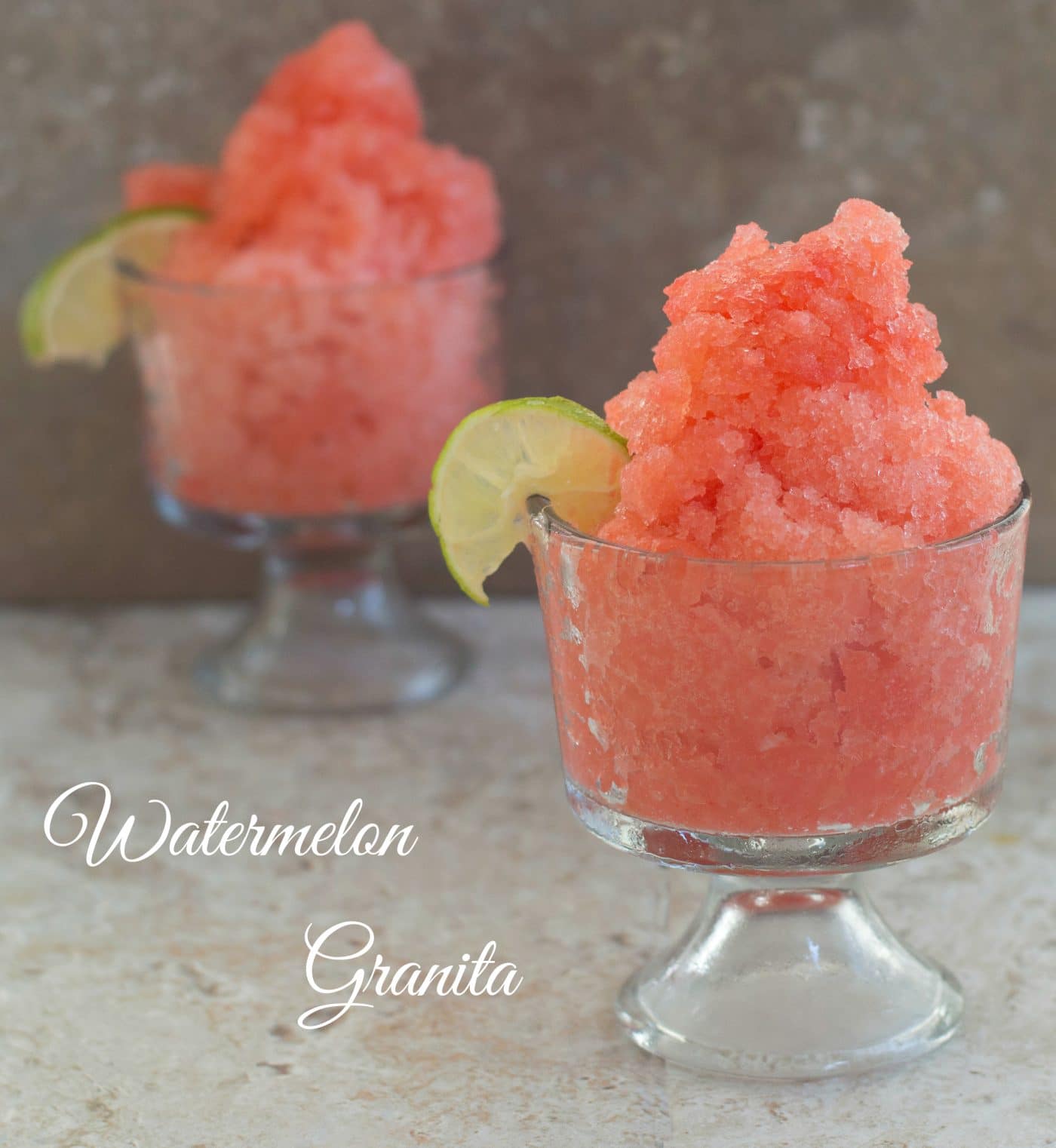 two small glass cups with watermelon granita and a wedge of lime