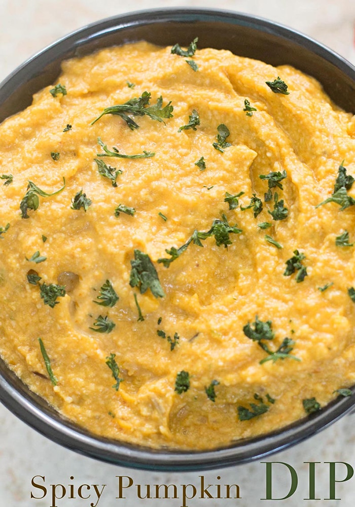 Closeup and Overhead View of a Black Bowl with Yellow Spicy Pumpkin Dip Garnished with Chopped Curley Parsley. 