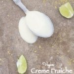 A Spoon Filled with Creme Fraiche is Laying Flat on a Brown Surface with the Liquid Spilled Around the Spoon. There are Slices of Lime and Nutritional Yeast Strewn Around