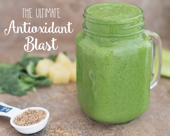 Front view of a glass filled with the ultimate antioxidant blast. Surrounded by flax seeds, pineapple and collard greens