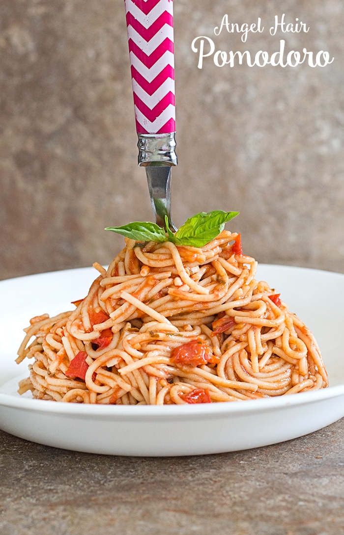 Thin Spaghetti in a White Bowl Arranged in a Cone Shape and A Fork With Chevron Pattern Handle Stuck on the Top of the Cone Shape. 2 Leaved Basil Next to the Fork For Garnish