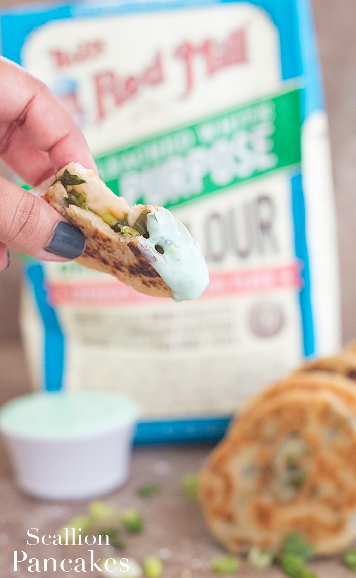 Closeup view of the author holding a piece of the scallion dipped in sauce