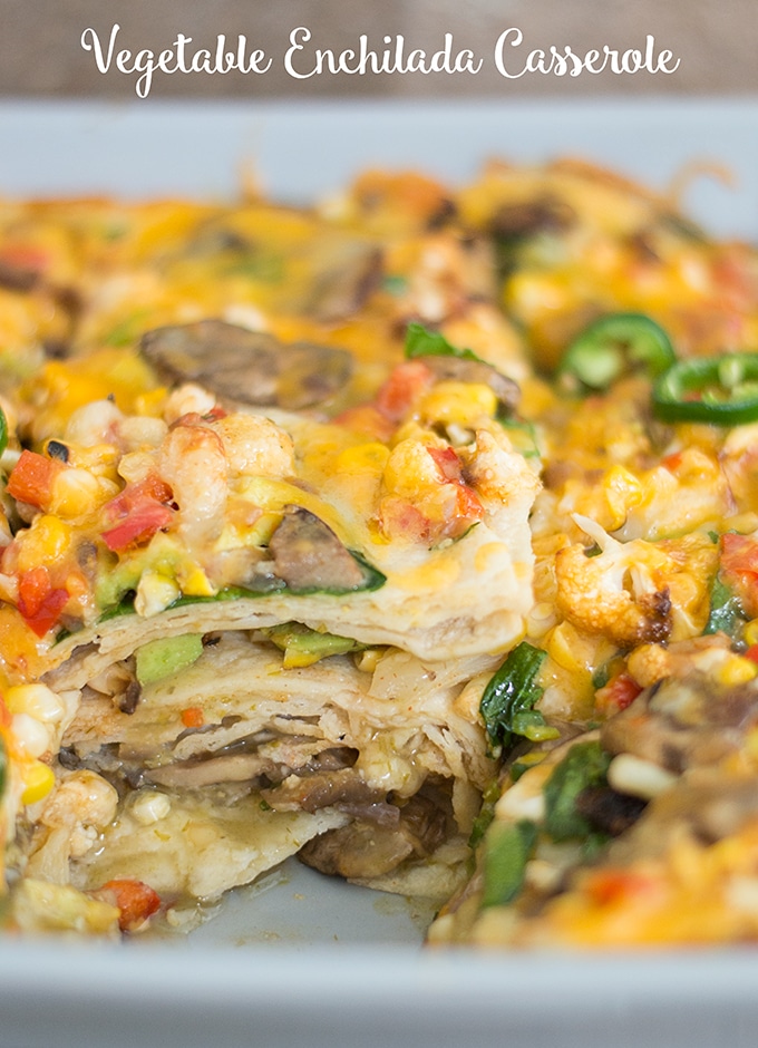 45 Degree View of the Casserole Dish. A Square Piece Has Been Removed From the Vegetable Enchilada Casserole In Order to get a View of the Layers. The Layers are Made up of Corn Tortillas and Roasted Vegetables. Topped with Melted Cheese, Corn and Jalapeño,