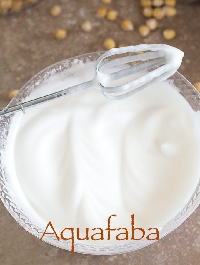 Overhead View of a Hand Mixer Beater Resting Diagonally on a Clear White Bowl Filled With Aquafaba. How To Make Aquafaba