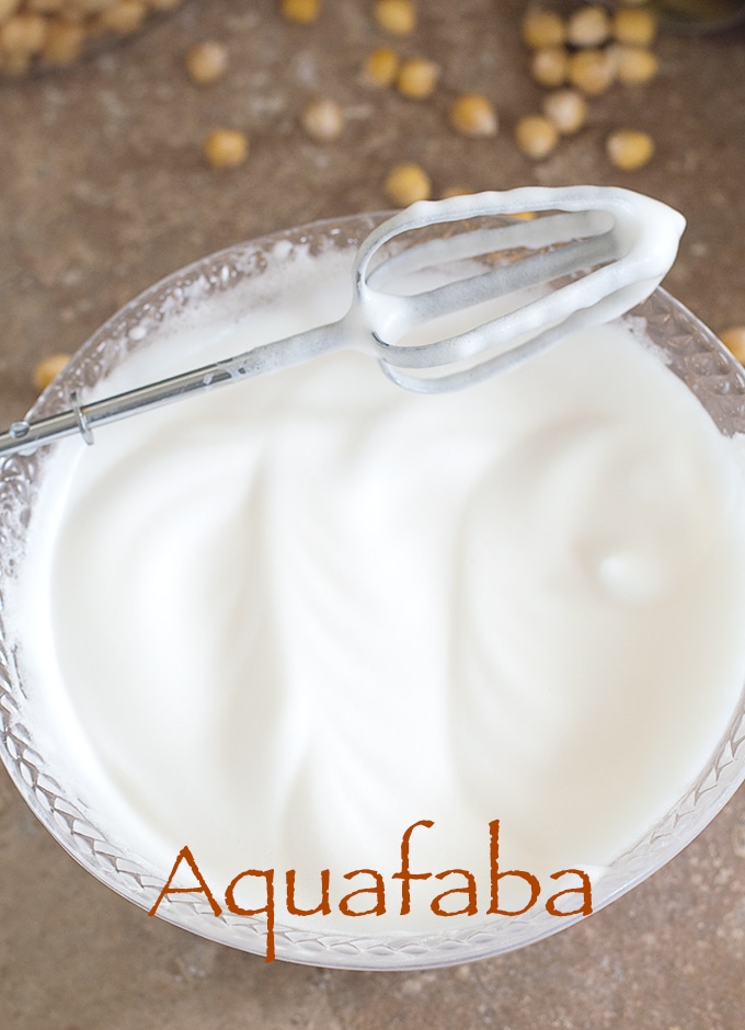 Overhead View of a Hand Mixer Beater Resting Diagonally on a Clear White Bowl Filled With Aquafaba. How To Make Aquafaba