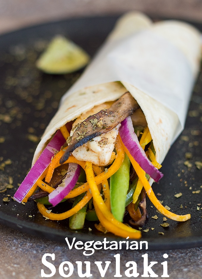 Front View of Butternut Squash Zoodles, Red Onions, Green Peppers, Feta, and Grilled Mushrooms Wrapped in a Tortilla and Placed on a Skillet. Oregano Strewn All Over. Pyramid-Shaped Lime is Visible in the Background - Vegetarian Souvlaki