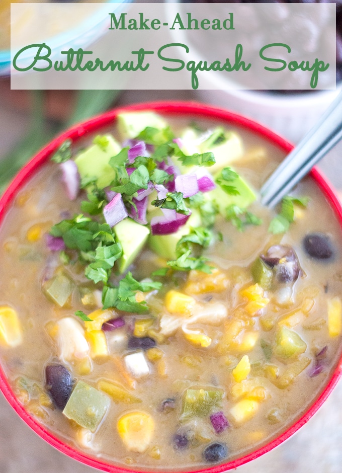 Overhead View of a Red Rimmed Bowl Filled with Butternut Squash Soup. Includes Black Beans, Corn, Green Bell Peppers and Liquid. One Side of the Soup Garnished with Avocado, Red Onions and Cilantro