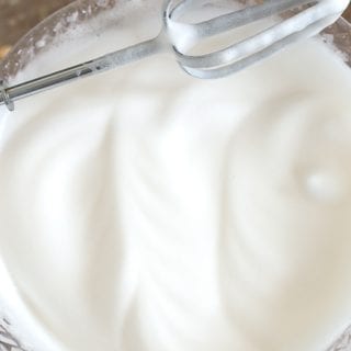 Overhead View of a Hand Mixer Beater Resting Diagonally on a Clear White Bowl Filled With Aquafaba. How To Make Aquafaba