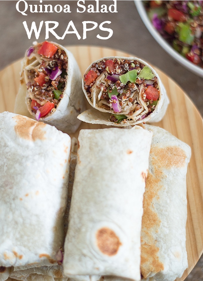 Overhead View of 5 quinoa wraps on a Brown Board. A 6th Quinoa Wrap is Cut Into Half and Placed Standing Up. The words "Quinoa Salad Wraps" visible. 