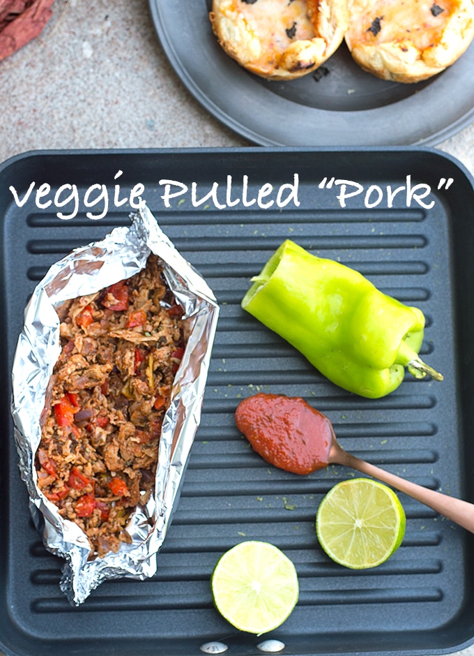 Overhead View of a Grill Pan with Veggie Pulled Pork in a Foil. Other Items on the Grill Include Half of a Cubanelle Pepper, Lime Halves and a Brass Spoon Filled with Pizza Sauce