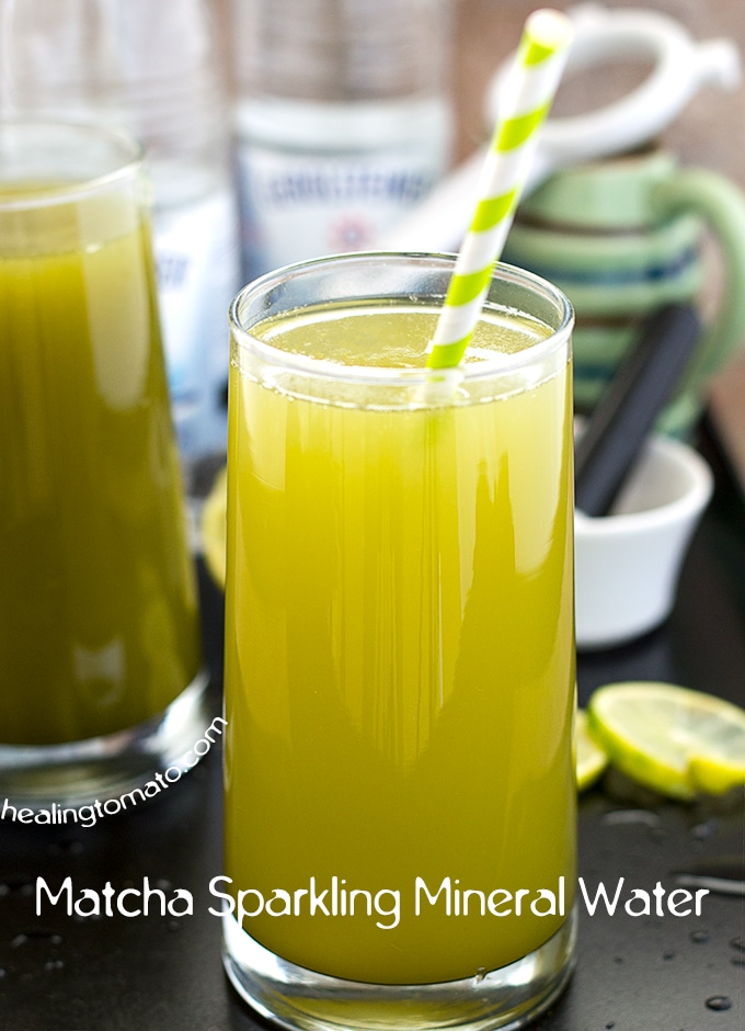 Front View of a Glass Filled with Matcha Water. Background has Gerolsteiner's Sparking Mineral Water and Small Ceramic Mug