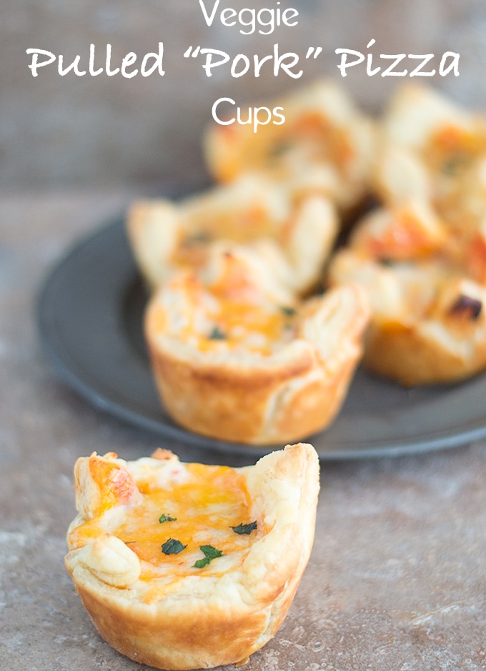 Front view of a Pizza Cup. In the Background, a Dark Grey Plate Filled with 5 Pizza Cups - Veggie Pulled Pork