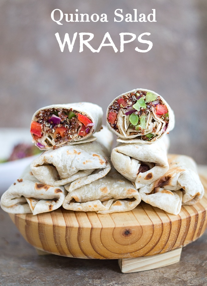 Front View of Five Wraps Placed on a Wooden Board. One Wrap is Cut Into Half and placed on Top. The words "Quinoa Salad Wraps" visible.  