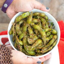Front view of the author's hands holding a white bowl filled with edamame pods