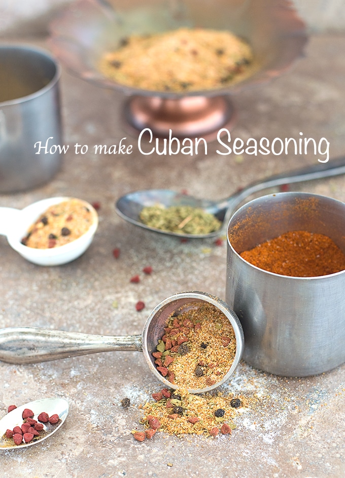 Front View of a vintage spoon filled with homamade Cuban seasoning and a small still bowl filled with cayenne pepper is in the back. Other spoons filled with different spices are visible in the background