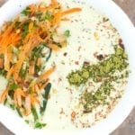 Closeup view of a white bowl filled with Tzatziki. It has carrot saalad on the left arranged in an arc and matcha powder line on the right.