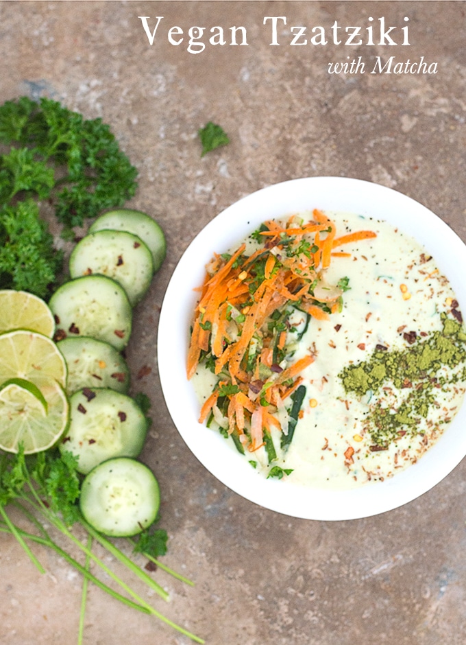 Closeup view of a white bowl filled with Tzatziki with carrot saalad on the left and matcha powder line on the right. To the left of the bowl, Parsley, cucumber and lime rounds are placed in an arc