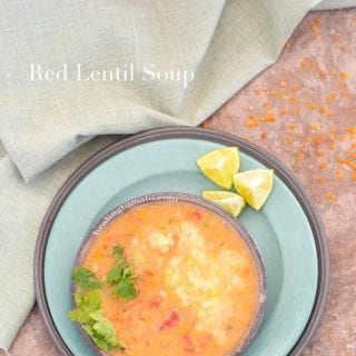 Overhead View of a Bowl With pressure cooker red lentil soup on A Green Plate. 3 Wedges of Lime on The Top of the Plate. A Green Cloth on the Left and Uncooked Red Lentils Around the Plate.