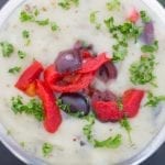 Closeup view of a steel bowl made filled with vegan Mediterranean mashed potatoes and topped with kalamata olives, bell pepper strips and fresh parsley