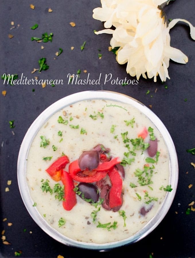 Overhead view of a steel bowl made filled with vegan Mediterranean mashed potatoes and topped with kalamata olives, bell pepper strips and fresh parsley