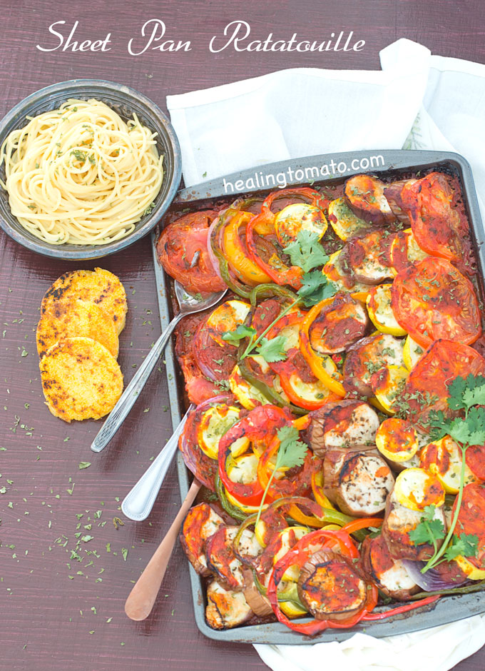 Overhead view of a Sheet Pan Filled With Ratatouille and 3 Spoons Coming Out at an Angle. A Grey Plate with Cooked Spaghetti is Visible on the Top